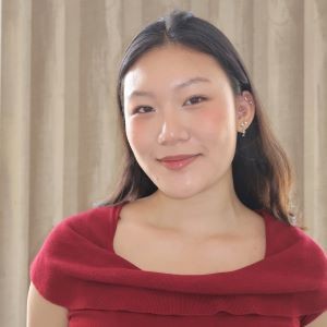 Leah Kim wearing a red shirt and standing in front of a beige background