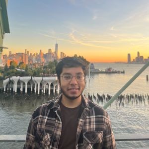 Qazi Ashikin standing in front in front of NYC skyline with beautiful sunset