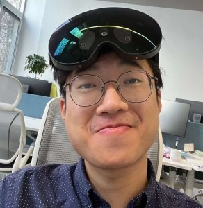Photo of Zihao Zhang sitting in a computer lab with a Meta Quest Pro on top of his head